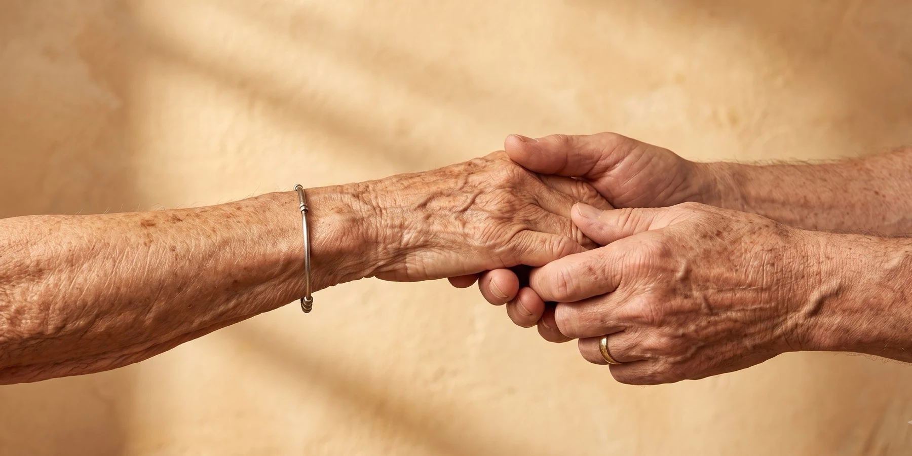 An older woman's hand held in the hands of her adult child.